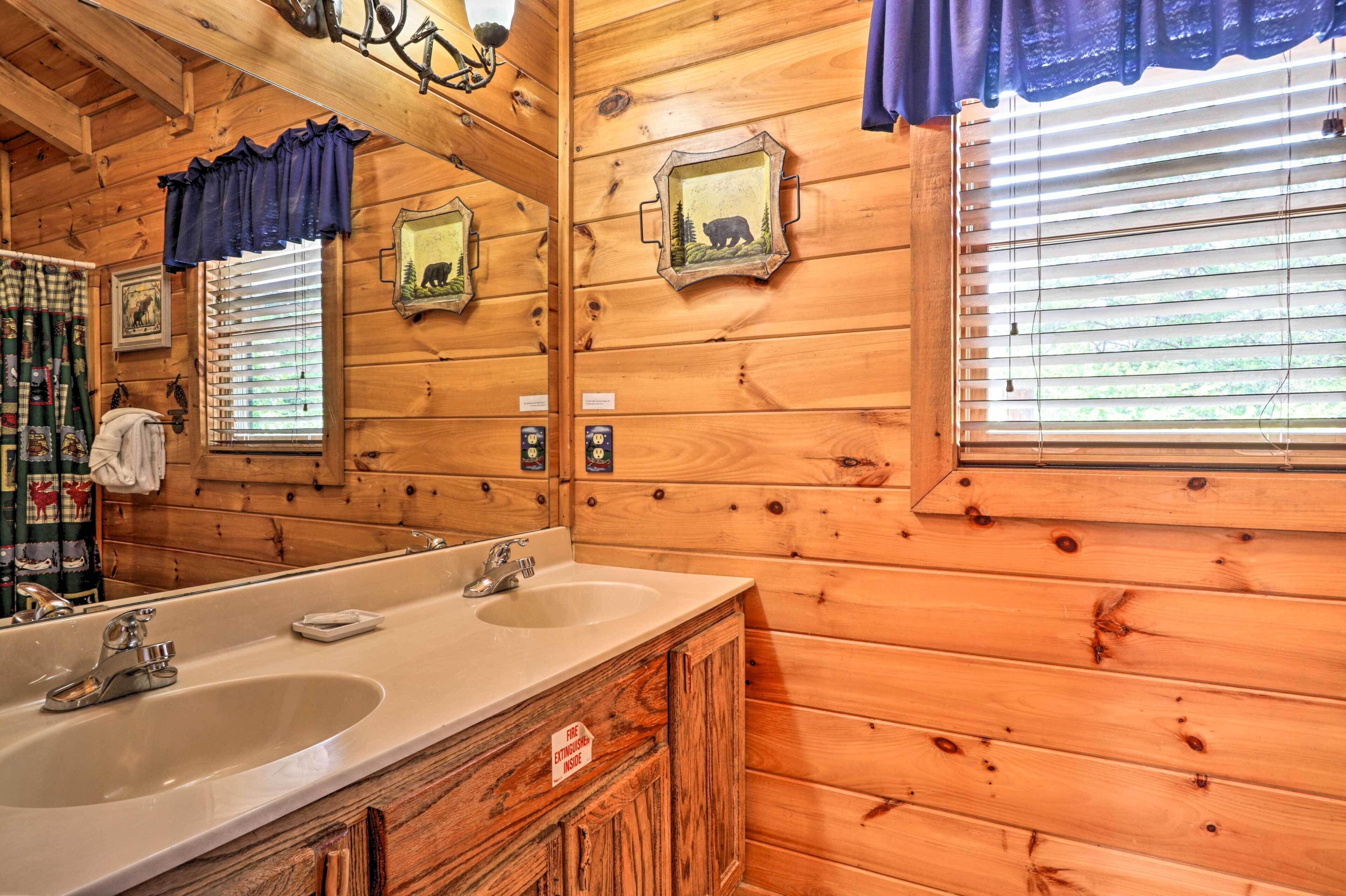 Baño de cabaña de madera con un lavabo grande, dos espejos y una ventana con persianas.