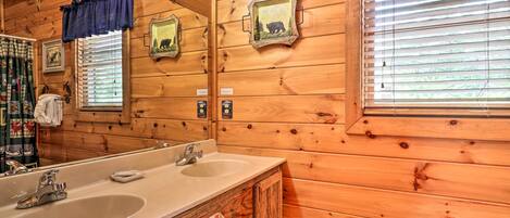 Baño de cabaña de madera con un lavabo grande, dos espejos y una ventana con persianas.
