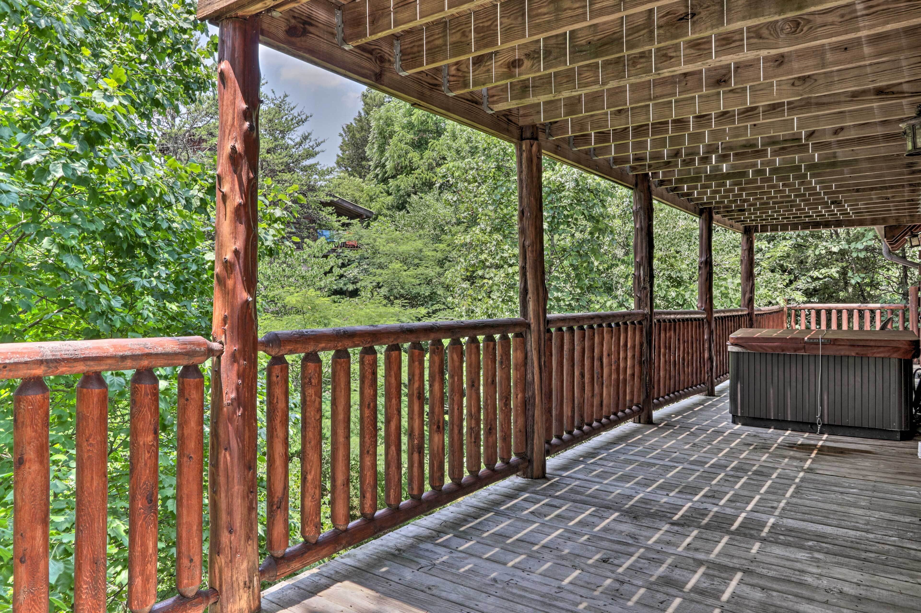 A wooden deck with a railing, a hot tub, and a view of a forested area.
