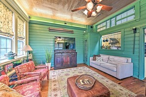 Una sala de estar acogedora con una pared verde, un sofá blanco, un tapete estampado y un ventilador de techo.
