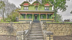 A two-story house with a porch, stone steps, and a carriage in the background.
