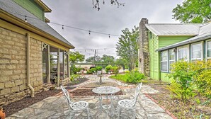 A patio area with a stone floor, two white metal chairs, a round table, and a string of lights.