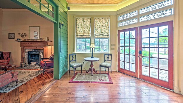 A room with a fireplace, a table with chairs, and large windows with decorative glass panes.