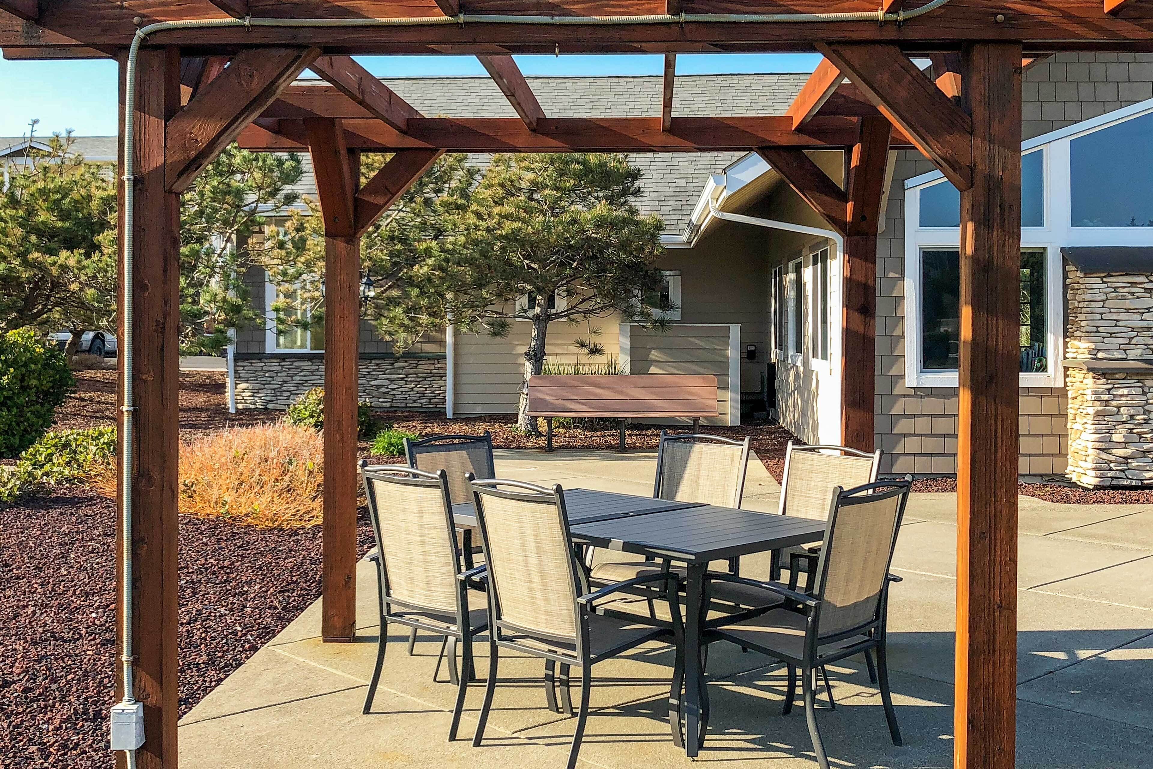 A covered patio with a table and chairs, a stone wall, and a house in the background.