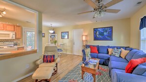A living room with a blue sofa, a wooden coffee table, and a ceiling fan. There is a kitchen area with a microwave and cabinets. - Beaufort Pad w/ Patio: 3 Blocks to Waterfront! (Beaufort)