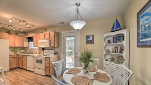 A modern kitchen with wooden cabinets, a white dining table with woven placemats, and a ceiling light fixture. - Beaufort Pad w/ Patio: 3 Blocks to Waterfront! (Beaufort)