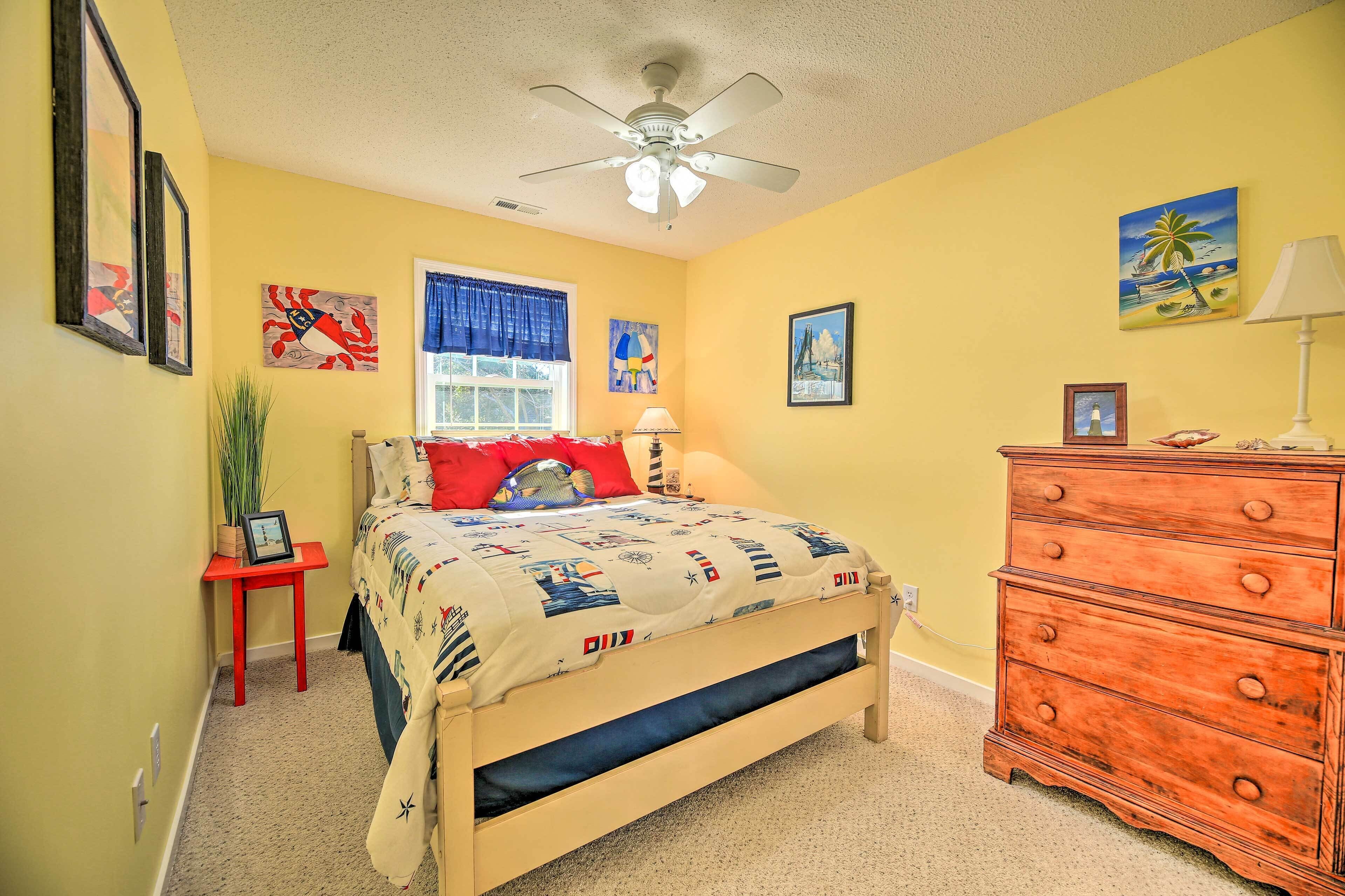 A bedroom with a bed, a dresser, a ceiling fan, and artwork on the walls.