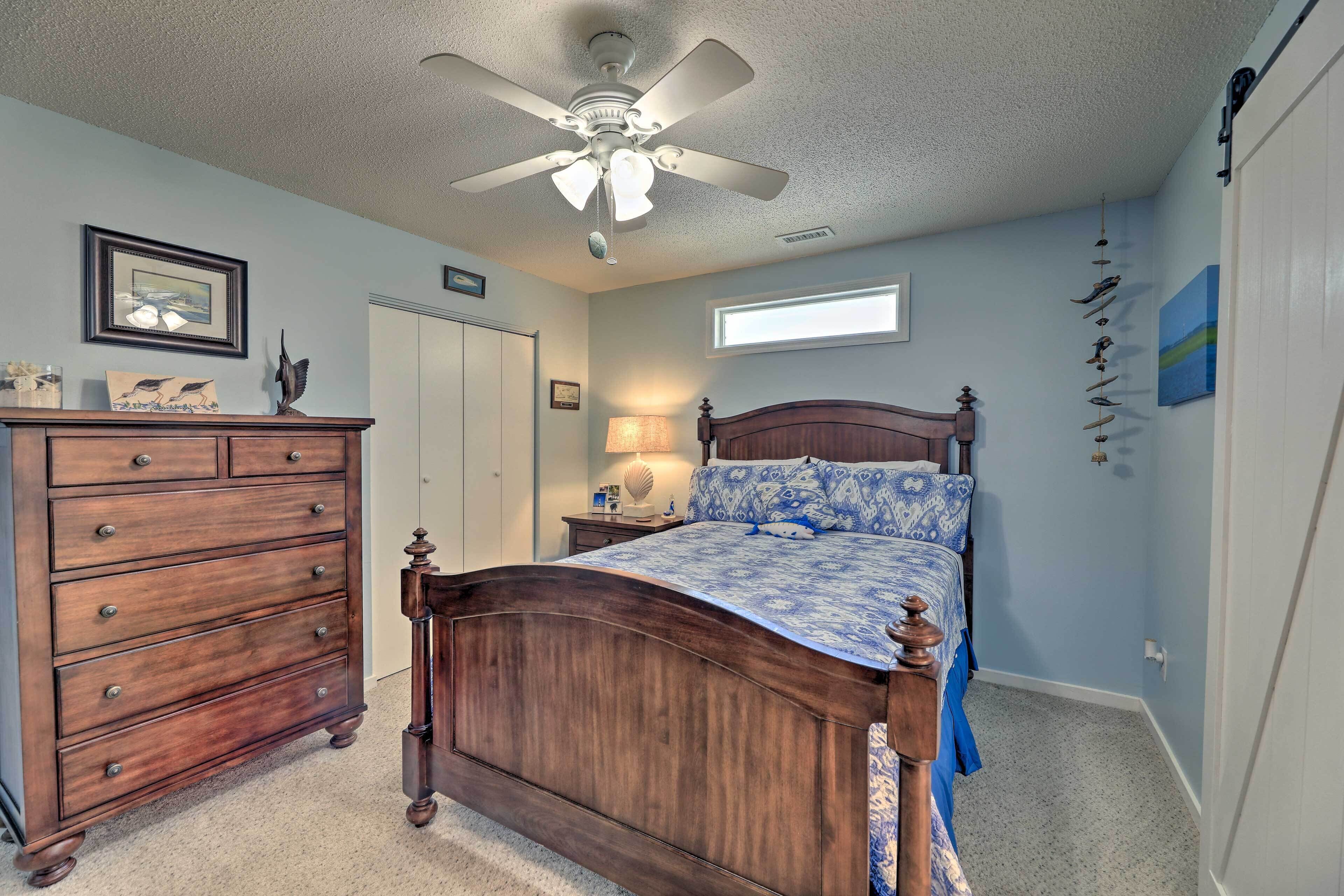 Un dormitorio con cama de madera, cómoda, ventilador de techo, ventana y decoración en la pared.