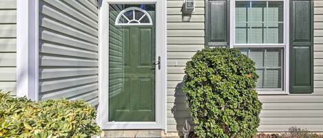 A house with a green door, a window with shutters, and a small bush in front.