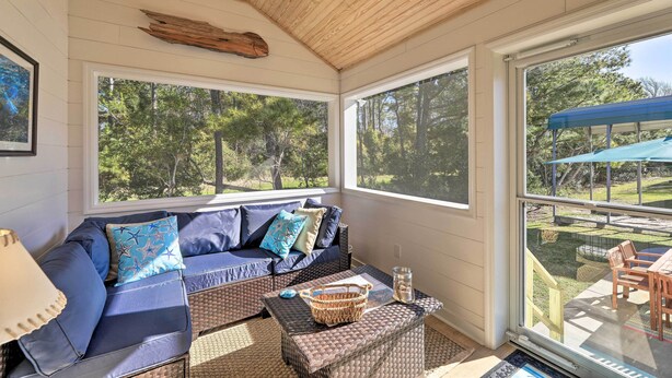 A sunroom with a large window, a blue sofa with star-patterned pillows, wicker furniture, and a ceiling fan. - Beaufort Pad w/ Patio: 3 Blocks to Waterfront! (Beaufort)