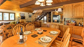Une table de salle à manger en bois, mise avec des assiettes, des verres et une bouteille, entourée de chaises en bois.