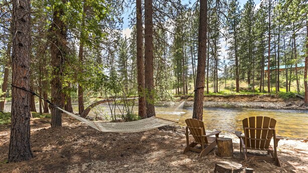 Un hamac tendu entre deux arbres, une chaise en bois et une table de pique-nique, le tout dans un espace boisé près d’une rivière.