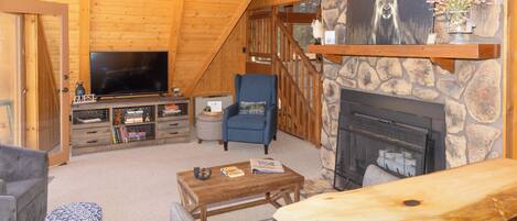 A cozy log cabin interior with a stone fireplace, a television, and a comfortable seating area.