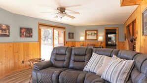 A cozy living room with a sectional sofa, wooden walls, and a ceiling fan.