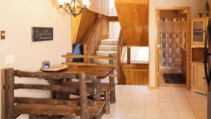 A wooden dining table with benches, a chandelier, and a staircase leading to a bathroom.