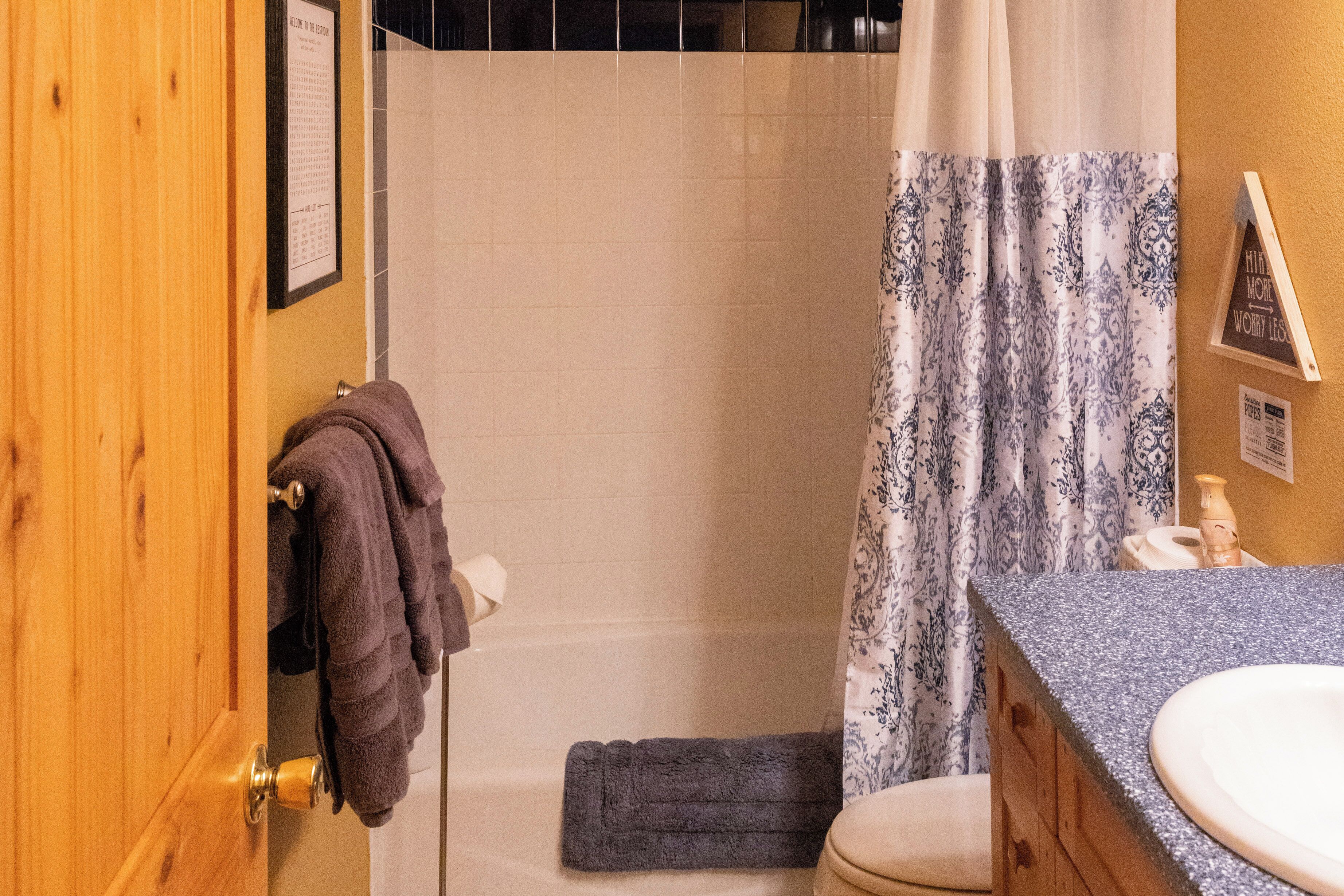 A bathroom with a wooden door, a shower with a curtain, a sink, and a towel rack.