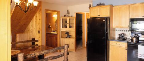 A kitchen with wooden cabinets, a black refrigerator, and a dining table with benches.