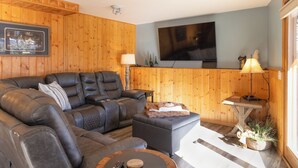 A cozy living room with a leather sofa, a flat-screen TV mounted on the wall, and a small table with a lamp.