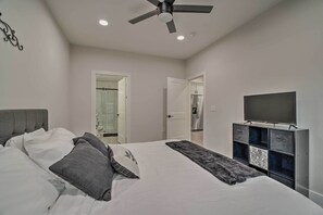 A bedroom with a bed, a ceiling fan, a TV on a cabinet, and a bathroom door. - Well-appointed Montgomery Home w/ Fenced Yard (Montgomery)