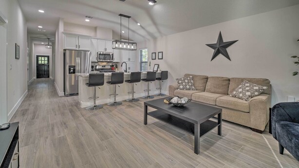 A modern kitchen with white cabinets, a stainless steel refrigerator, and a bar area with black bar stools. - Well-appointed Montgomery Home w/ Fenced Yard (Montgomery)