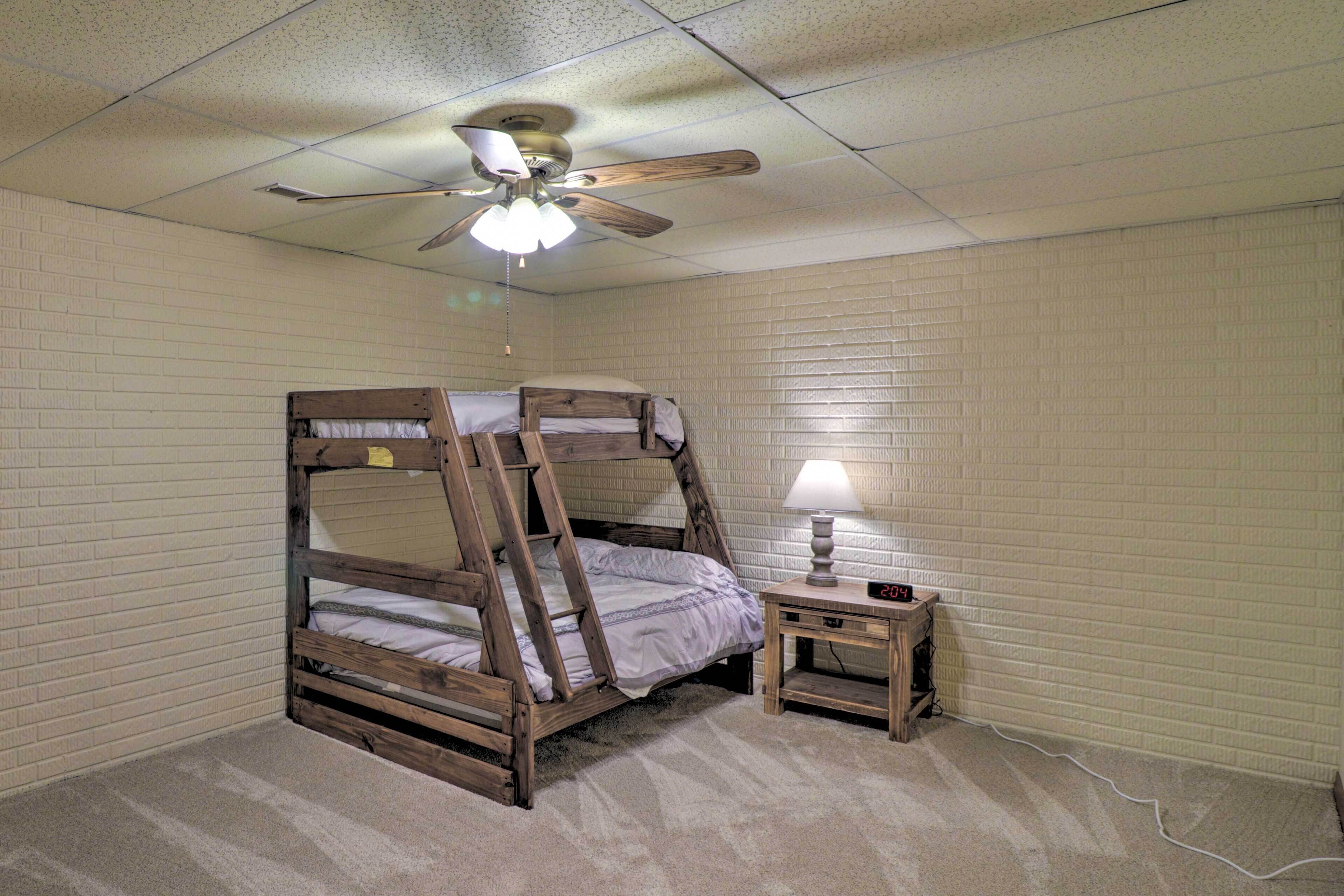 A bunk bed room with a ceiling fan, a nightstand with a lamp, and a brick-patterned wall.
