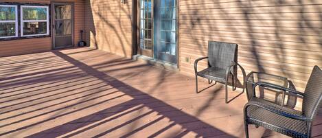 Une terrasse couverte avec deux fauteuils en osier, une porte-fenêtre coulissante et un petit espace extérieur où un outil en métal est appuyé contre le mur.