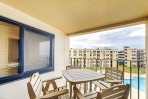 Varanda com mesa, cadeiras, janela e vista para uma piscina e edifícios.