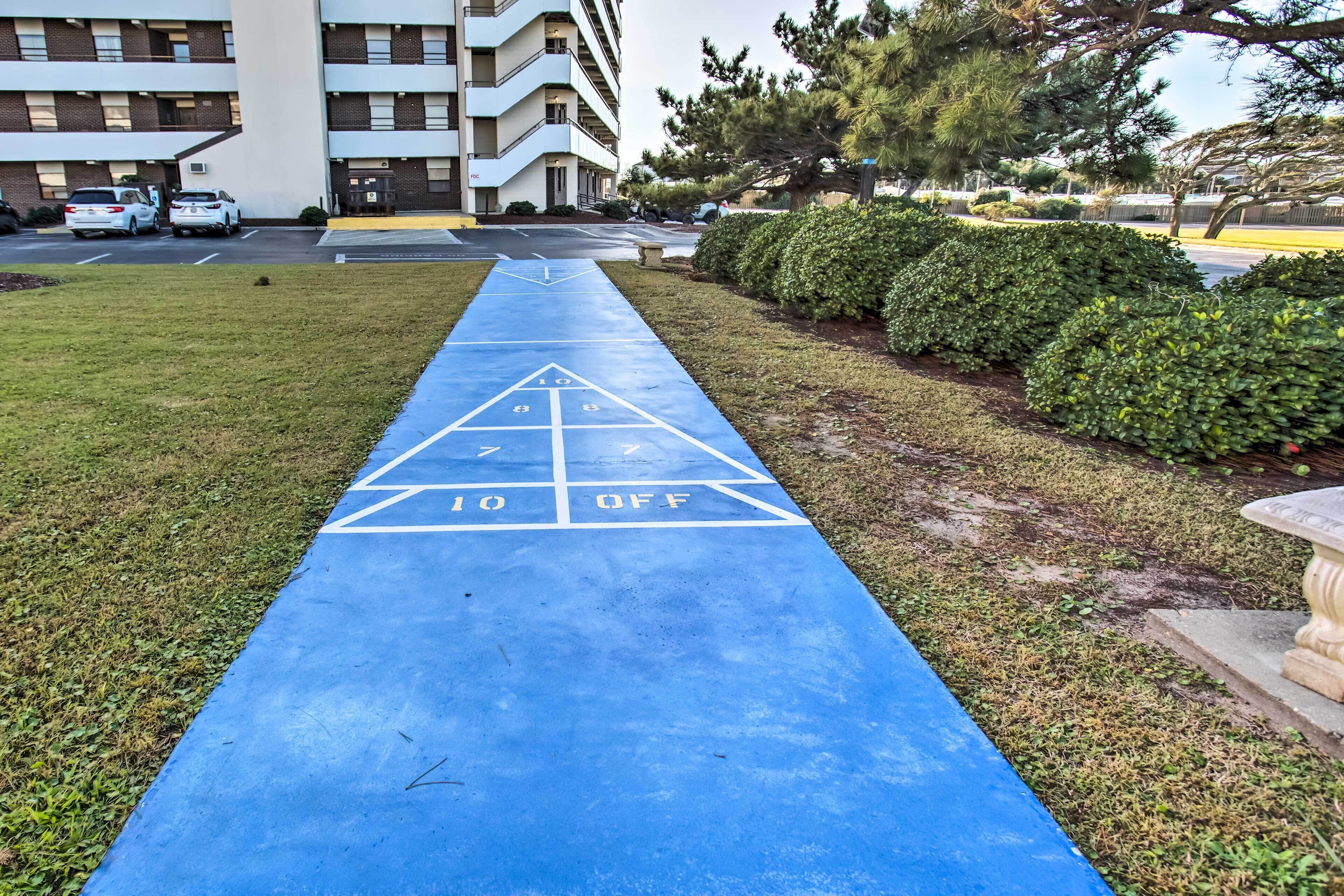 Un terrain de jeu de «shuffleboard» bleu, avec une zone de 10 x 10 pieds délimitée, entouré de pelouse et d’une haie.