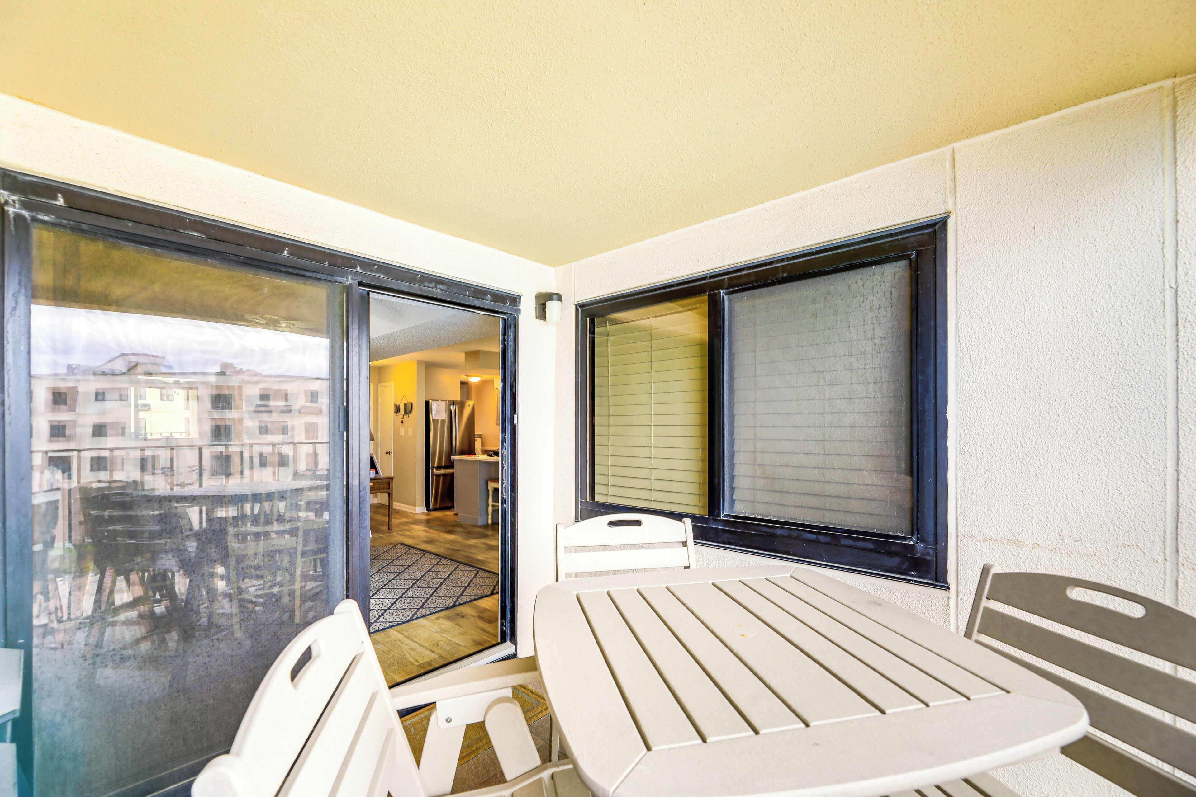 Ein Balkon mit Tisch und Stühlen, eine Schiebetür und Blick auf ein Gebäude.