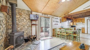 Un accogliente interno di una baita con parete in pietra, stufa a legna, zona pranzo e cucina.