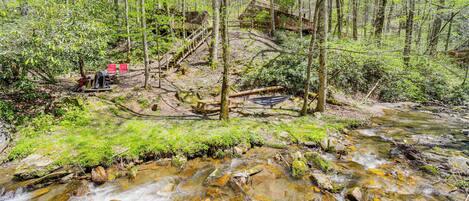 A forest stream with a wooden bridge and picnic table.