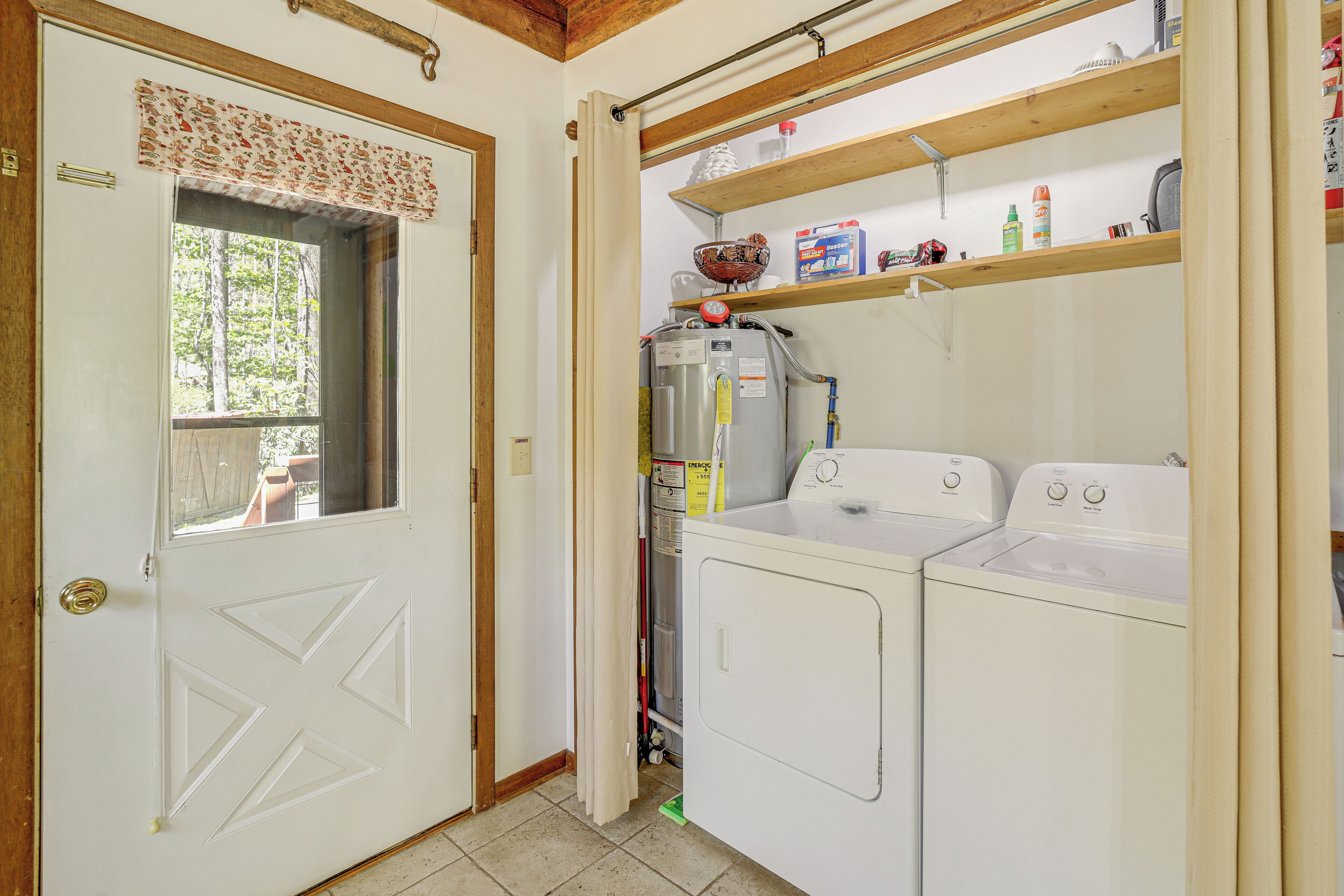 A laundry room with two white washing machines, a dryer, and shelves above holding various items.