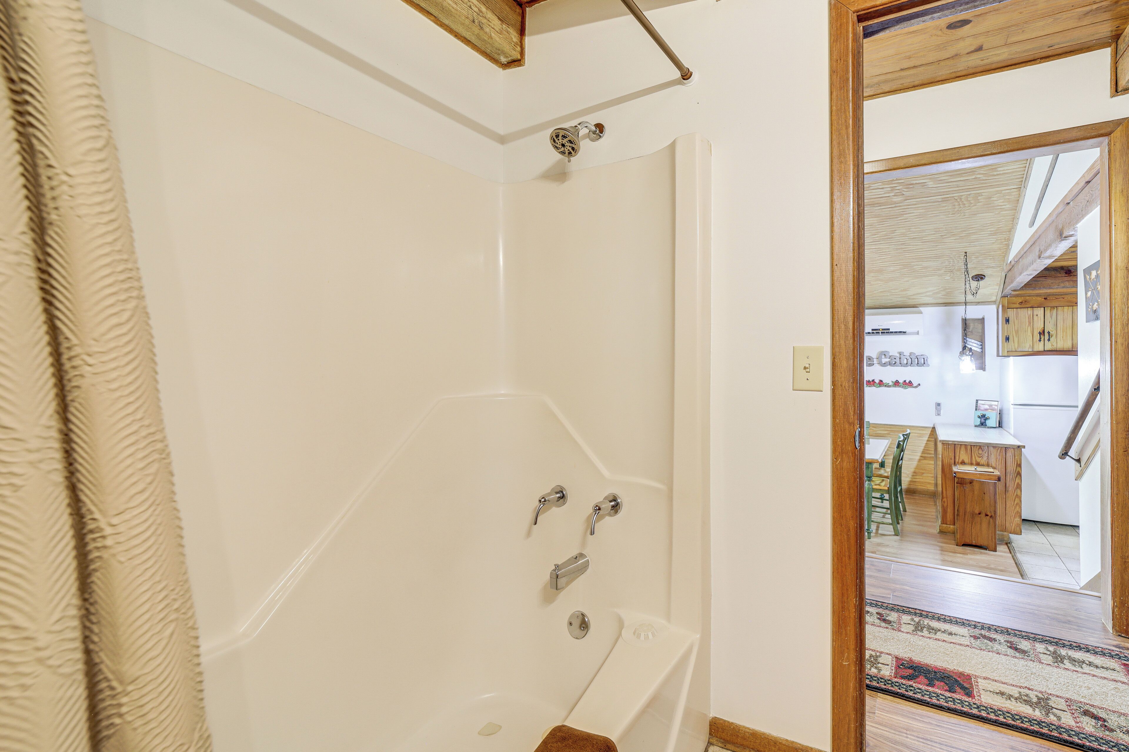 A bathroom with a bathtub, shower, and a wooden door leading to a kitchen area.