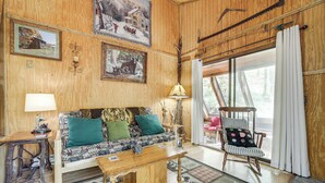 Un accogliente soggiorno con finiture in legno, un divano a fantasia, un tavolino in legno e una poltrona a dondolo vicino a una grande finestra.