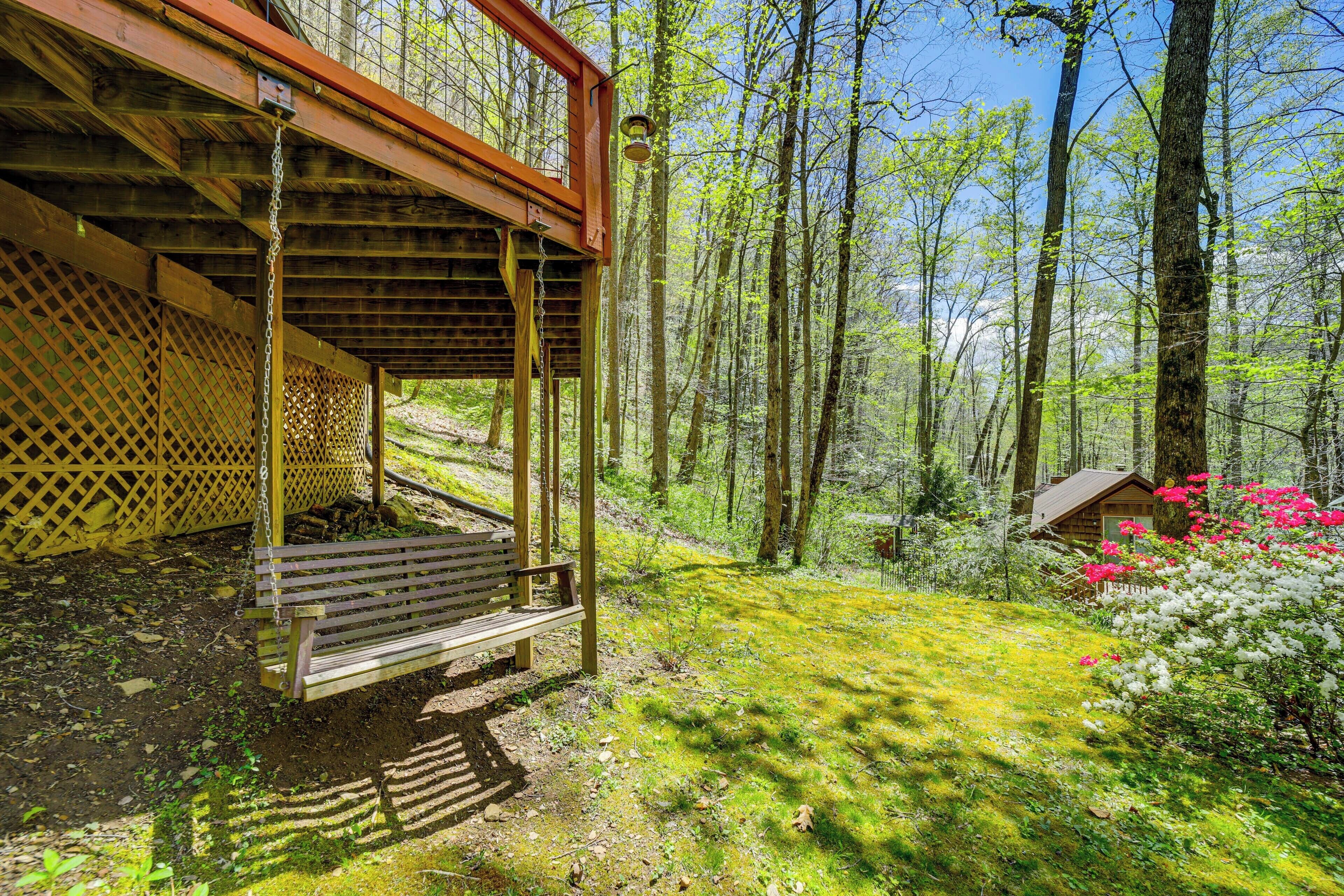 Eine hölzerne Pergola mit einer Bank, umgeben von einem Wald mit hohen Bäumen und blühenden Blumen.