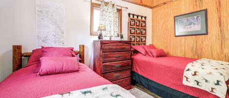 Un dormitorio con dos camas, paredes de madera, un aparador y un mapa colgado en la pared, junto con un cuadro enmarco.