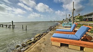 A beachside view with wooden lounge chairs and a pier in the background. - Bayfront Deck: 'casa Pescadores' Rockport Escape (Rockport)