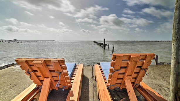 Two wooden lounge chairs with blue cushions on a concrete platform by the water, with a pier extending into the sea in the background. - Bayfront Deck: 'casa Pescadores' Rockport Escape (Rockport)