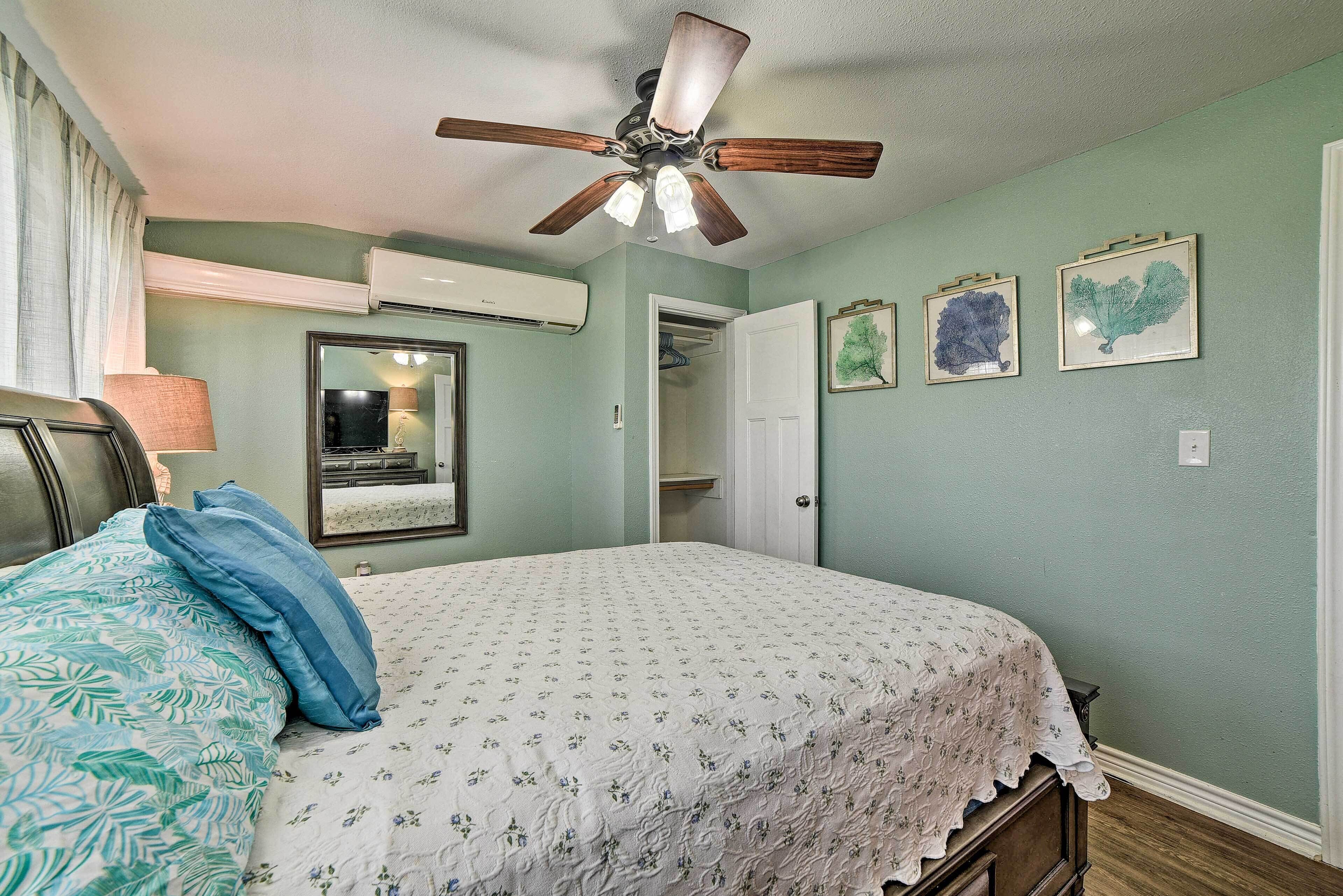 A bedroom with a bed, ceiling fan, air conditioning unit, and framed botanical prints on the wall.