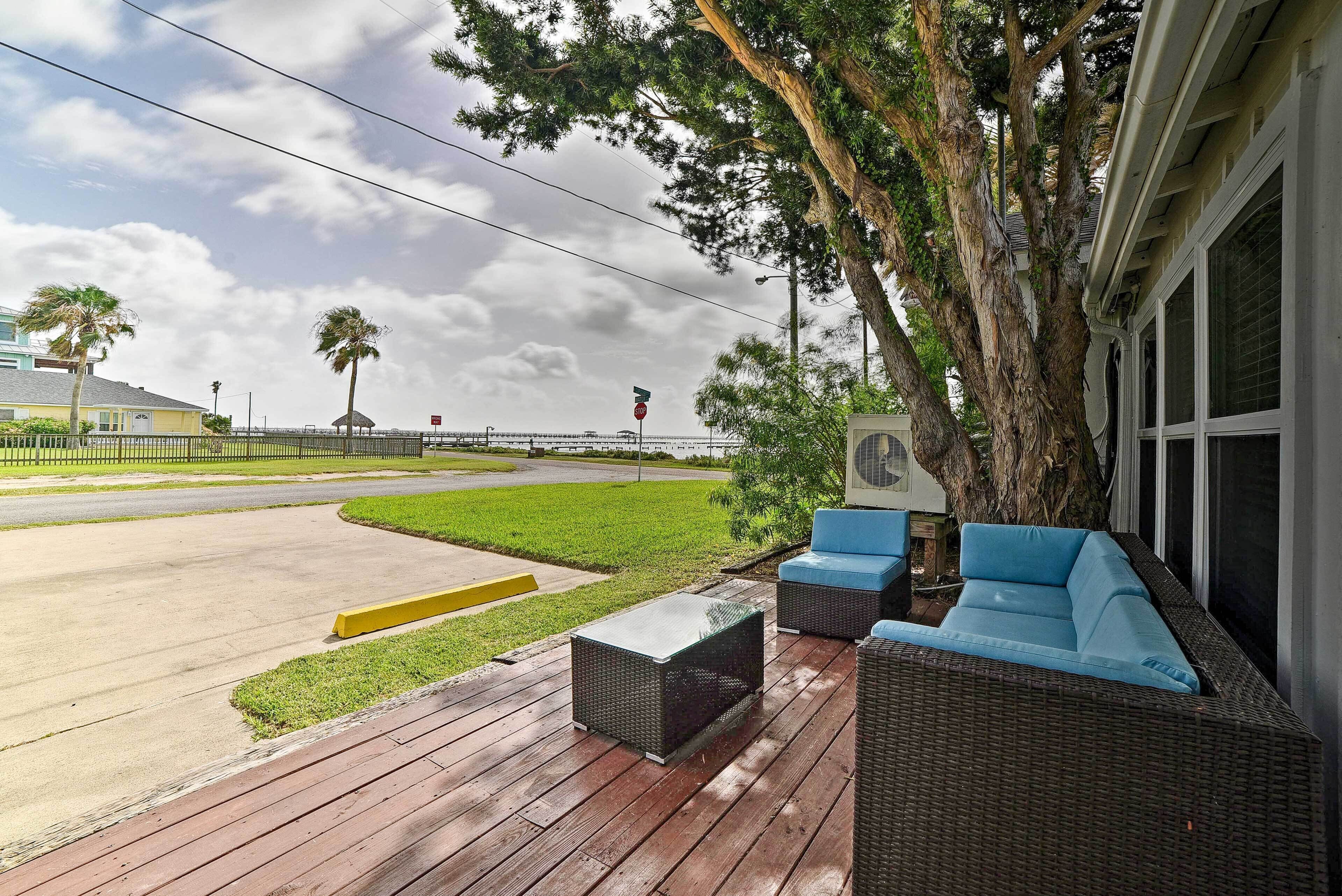 Terraza exterior con mobiliario de mimbre y un árbol grande, con vista a una carretera y zona verde.