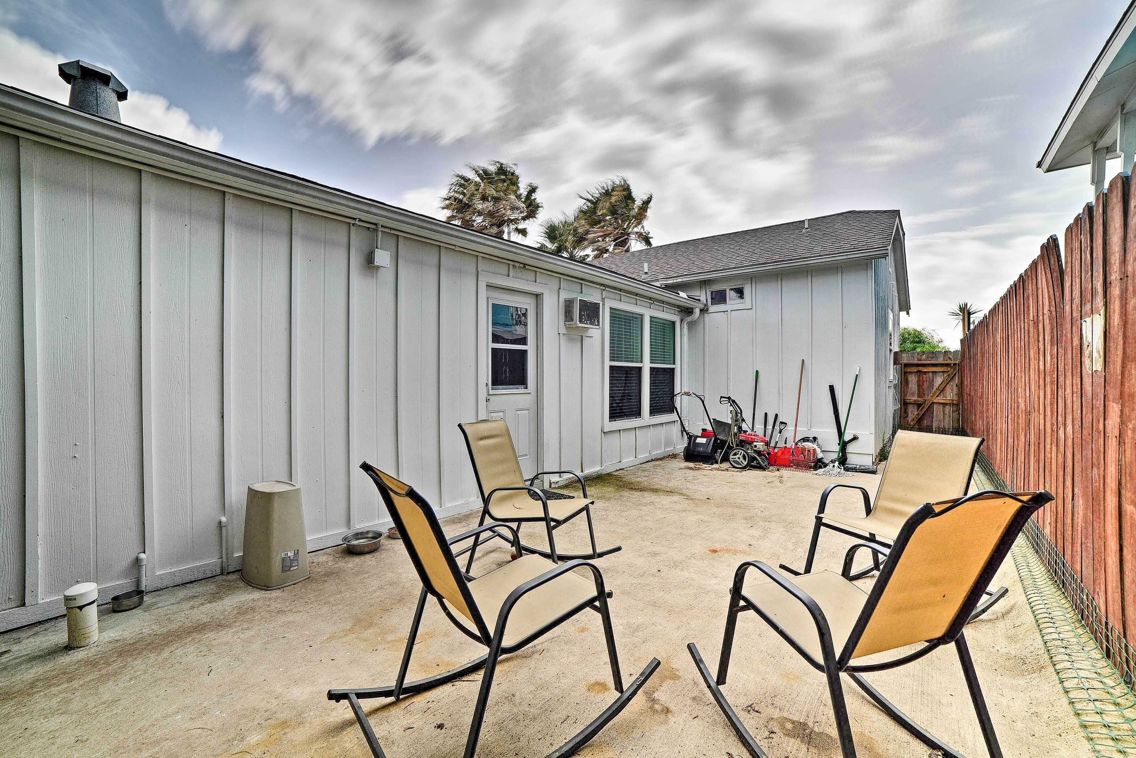 A backyard with a white building, two rocking chairs, a dog bowl, and a trash can.