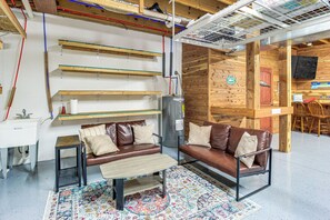 A cozy living area with a brown leather sofa, a small coffee table, and a colorful rug. There are wooden shelves and a white sink in the background. - Modern Tims Ford Lake Home w/ Private Dock & Pool! (Lynchburg)