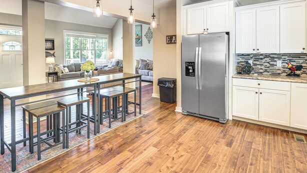 A modern kitchen with white cabinets, a stainless steel refrigerator, and a wooden dining area with stools. - Modern Tims Ford Lake Home w/ Private Dock & Pool! (Lynchburg)