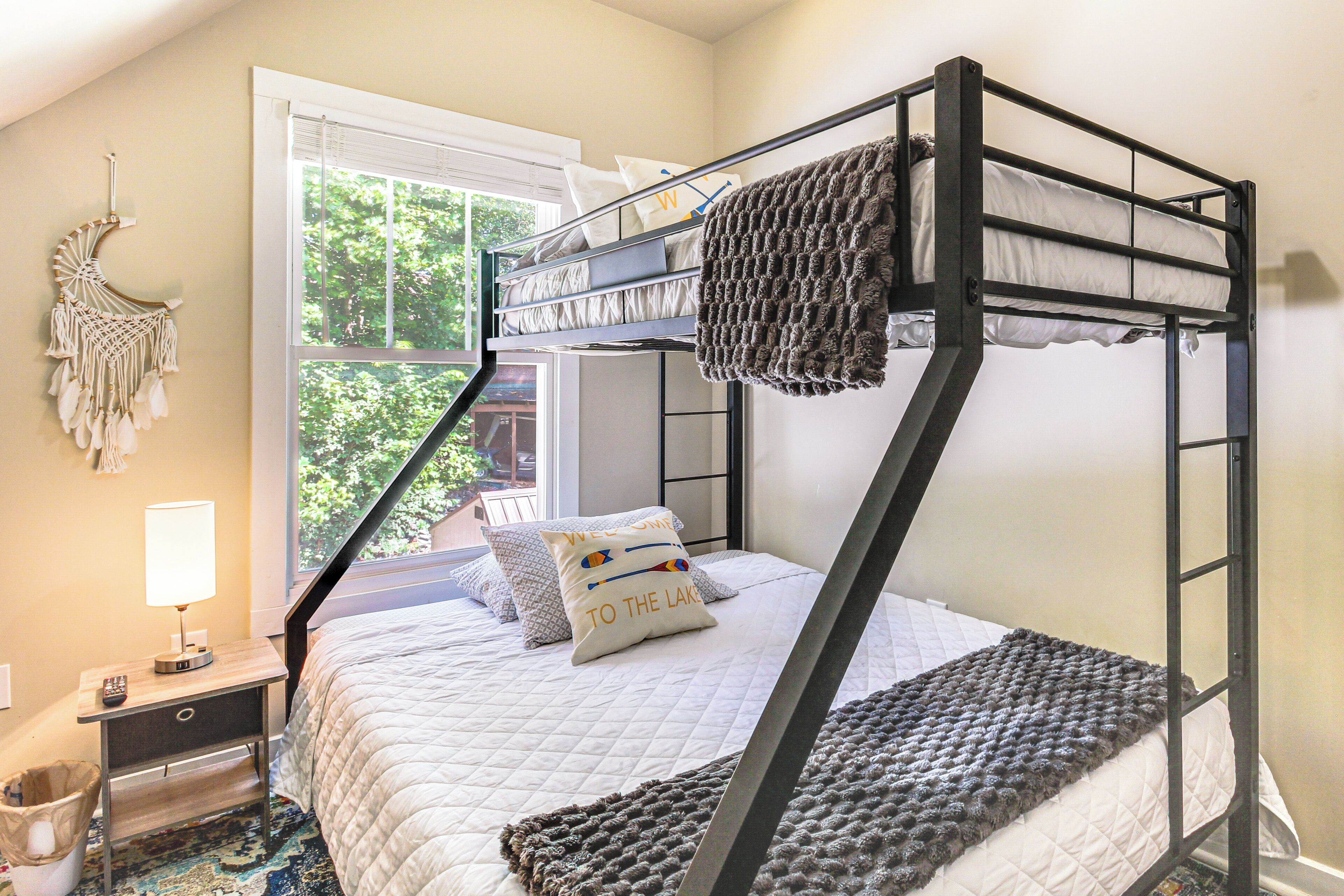 A bunk bed with a white quilt, a macrame wall hanging, and a window with a view of trees.