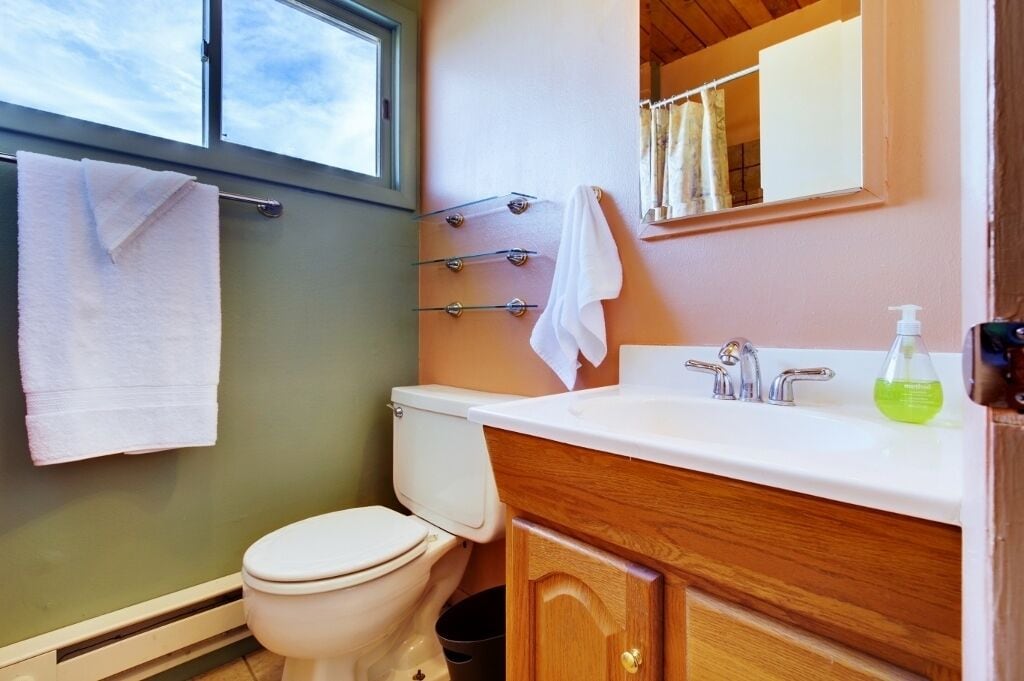 A bathroom with a toilet, a sink with a mirror, and a window above the toilet.