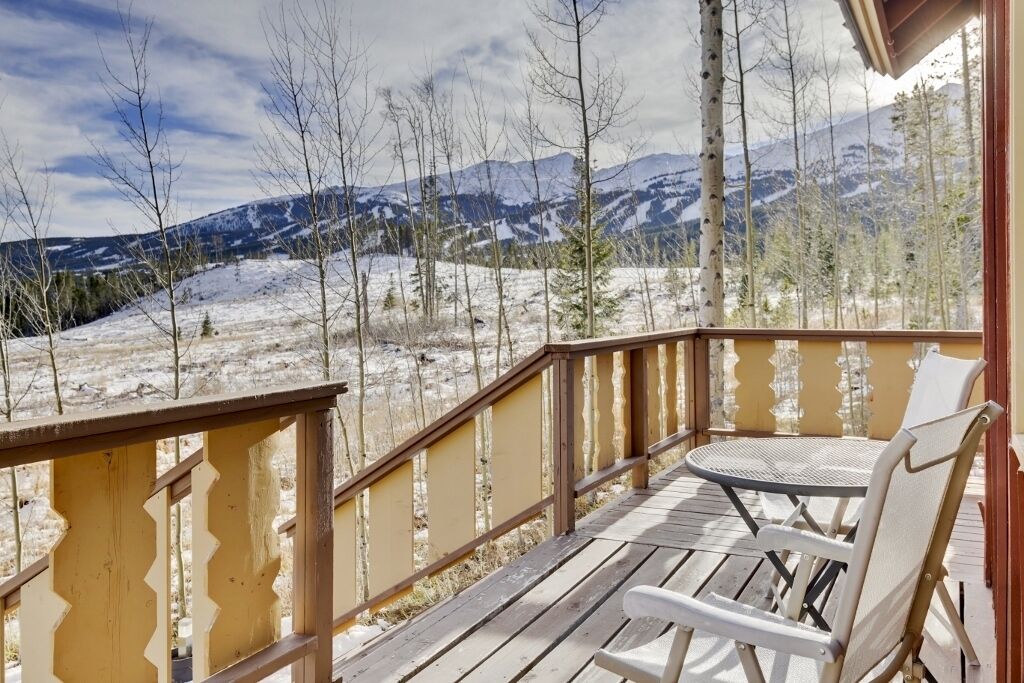 Eine Holzterrasse mit Tisch und Stühlen mit Blick auf eine verschneite Berglandschaft.