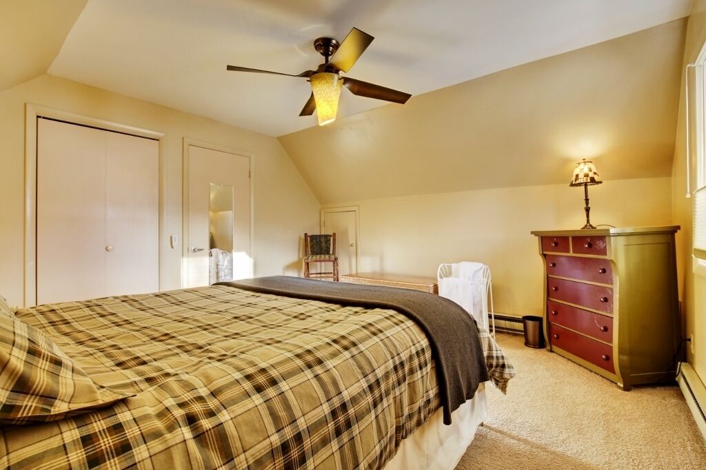 A bedroom with a bed, a dresser, a chair, and a ceiling fan.