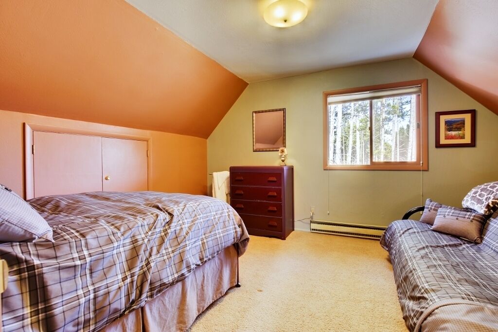 Une chambre avec deux lits, une commode, une fenêtre donnant sur des arbres et un luminaire au plafond.