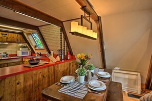 A dining area with a wooden table set for four, a red countertop, and a hanging light fixture above. - Ski Chalet on Saco < 2 Mi To Attitash Resort! (Bartlett)