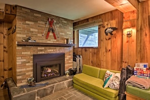 A cozy living room with a fireplace, wooden walls, a green sofa, and ski equipment. - Ski Chalet on Saco < 2 Mi To Attitash Resort! (Bartlett)